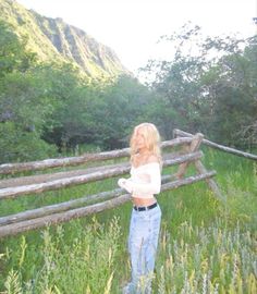 a woman standing in tall grass next to a wooden fence