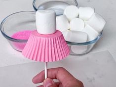 a hand holding a marshmallow lollipop over a bowl of pink sugar