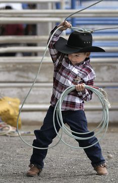 a young boy holding onto a rope while wearing a cowboy hat