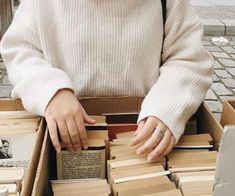 a woman standing in front of a box filled with books