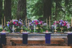 a long table with purple and pink flowers on it is set up for an outdoor dinner