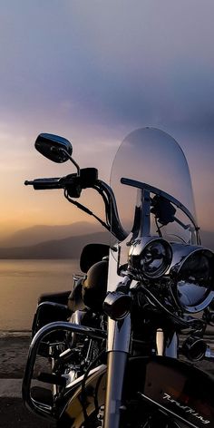 a motorcycle parked next to the ocean at sunset