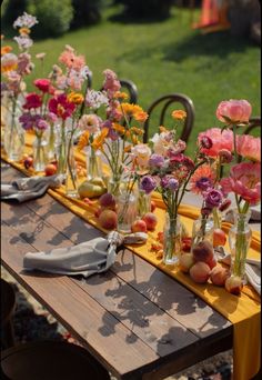 a long table topped with lots of vases filled with different types of flowers and fruit