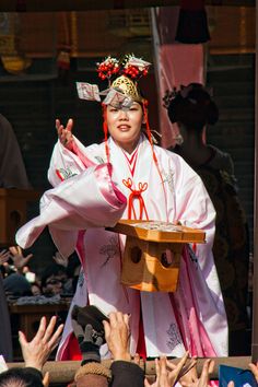 a woman dressed in traditional japanese garb and holding a box with her hands up