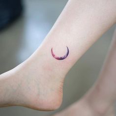 a small crescent tattoo on the foot of a person's left foot, with an inked moon in the middle