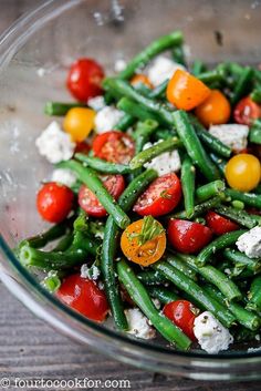 a glass bowl filled with green beans, cherry tomatoes and feta cheese on top