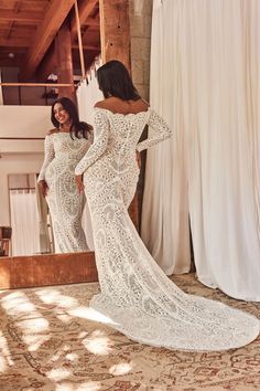 two women standing in front of a mirror looking at their wedding gowns on display