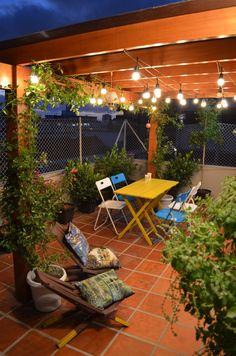 an outdoor patio with lights and plants on the table, chairs and tables in the background