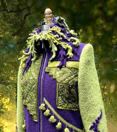 a green and purple jacket on a mannequin's head with trees in the background