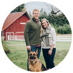 a man and woman standing next to a large dog in front of a red barn