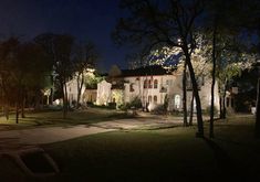 a large white house lit up at night with trees in the foreground and lights on