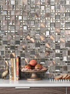 a table topped with books next to a wall covered in silver tiles and fruit on top of it