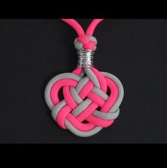 a pink and grey necklace with a silver heart charm on a black background is shown