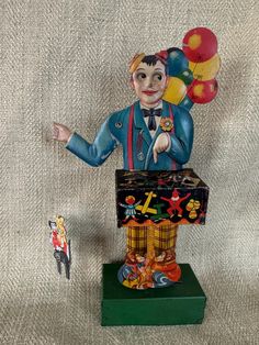 a clown figurine with balloons on it's head and a box in the foreground