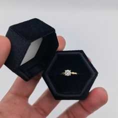 a hand holding an open ring box with a diamond in it's right hand