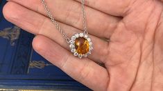 a person is holding a necklace with an orange stone and white diamonds in the center