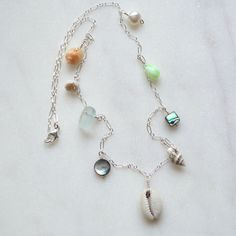 "This beautiful ocean inspired necklace features a sliced cowrie shell in the center with various shells, a white pearl and frosted glass dangling from a sterling silver 1.6mm long and short chain. Available in 18\" or 24\" lengths. Shells include pyrene, nassa, abalone, tapok, puka Also available in gold filled" Silver Shell Jewelry With Pearl Charm, Silver Necklaces With Charms For The Beach, Silver Necklace With Pearl Charm For Beach, Beach Jewelry: Silver With Pearl Charm, Beach Jewelry With Silver Pearl Charm, Silver Beach Jewelry With Pearl Charm, Beach Silver Jewelry With Pearl Charm, Silver Jewelry With Pearl Charm For Beach, Silver Dangle Jewelry With Shell