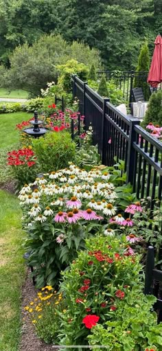 a garden filled with lots of colorful flowers next to a black metal fence and umbrella