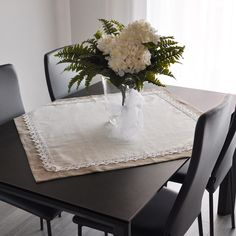 a vase with white flowers sitting on top of a wooden table next to black chairs