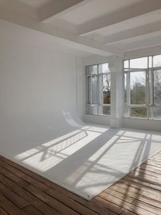 an empty room with wooden floors and large windows on the wall, in front of white walls