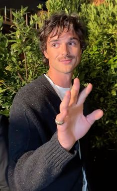 a young man making the vulcan sign with his hand while standing in front of some bushes