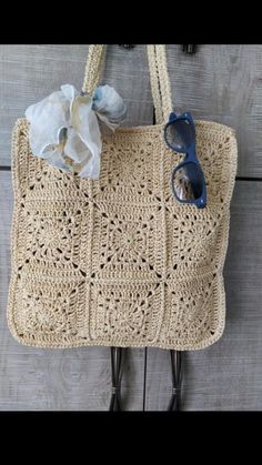 a crocheted bag hanging on a wall with sunglasses and a flower in it