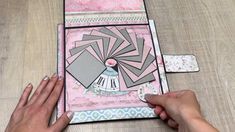 someone is making a card with pink and grey paper on it, while another person's hands are holding the edge of the card