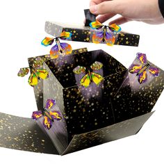 a hand holding a black box with purple and yellow butterflies on it, flying out of it