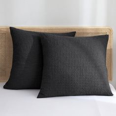 two black pillows sitting on top of a bed next to a wicker headboard