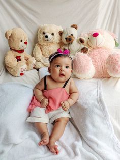 a baby sitting on a bed surrounded by teddy bears and other stuffed animals, all looking at the camera