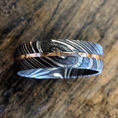 This is a USA made comfort fit 7mm wide Damascus Steel with a rounded top profile, acid etch, and 1 millimeter center 14k Rose Gold inlay is simply stunning. It is very comfortable to wear with a rounded comfort fit design. This ring is hand finished & designed by jewelry artisans who have a passion Damascus Steel Wedding Band, Damascus Ring, Damascus Steel Ring, Mens Wedding Rings, Men's Rings, Damascus Steel, Steel Ring, Damascus, Mens Wedding Bands