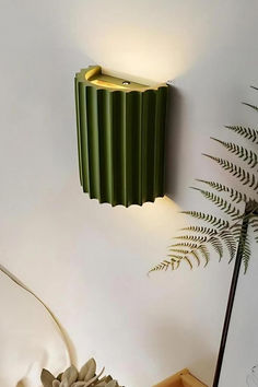 a green lamp on the wall next to a potted plant