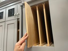 a hand is pointing at the open cabinet doors on a kitchen countertop with gray cabinets in the background