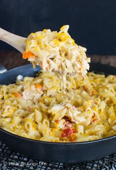 a spoon full of macaroni and cheese being lifted with a wooden spatula