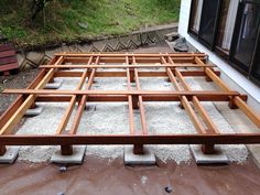 a wooden bed frame sitting in the middle of graveled area next to a building