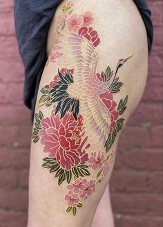 a woman's thigh with flowers and a bird tattoo on her leg, in front of a brick wall