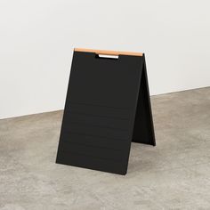 a black sign sitting on top of a cement floor next to a white wall in an empty room