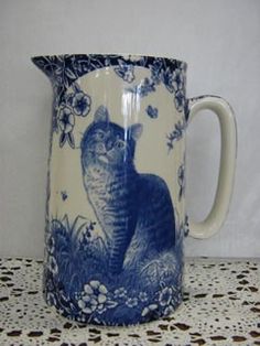 a blue and white coffee mug with a cat on it's side sitting on a doily