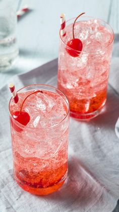 two glasses filled with ice and cherries on top of a table next to silverware