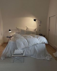 a bed with white sheets and pillows in a bedroom next to a lamp on the wall