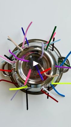 a bunch of colorful toothbrushes sticking out of a metal strainer on top of a white surface