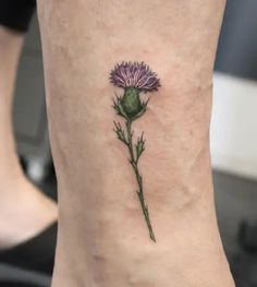 a small purple flower on the side of a woman's leg with green leaves