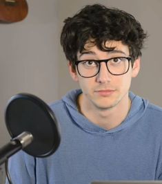 a young man with glasses is looking at the camera in front of a computer screen