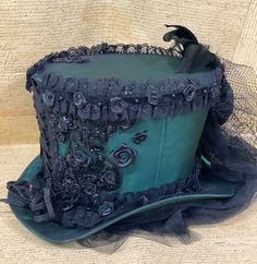 This is elegant Victorian gothic Hand made Bottle green satin Top hat with black back beautifully hand crafted feathers and bows black net bustle train.Top Hat with Black laces and 3D silk flowers and black pearls and jewels and sequences hand stitched. There is brass buckle at the side.Please refer to the photos.This is stunning Victorian Steampunk Handmade top hat made with lots of love.It is very well made, this hat is made of a Black satin type of fabric and the inside of the hat is has a Bl Fitted Fantasy Costume Hats For Themed Events, Gothic Top Hat With High Crown For Parties, Fitted Steampunk Top Hat For Halloween, Fitted High Crown Top Hat For Cosplay, Fitted Black Top Hat For Costume, Black Fitted Top Hat For Costume, Fitted High Crown Hat For Carnival, Vintage Fitted Top Hat For Cosplay, Fitted Vintage Costume Hats And Headpieces For Cosplay