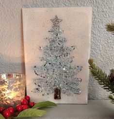 a lit christmas tree is displayed on a shelf next to a candle and some berries