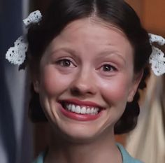 a smiling woman in a white dress with crochet hair clips on her head