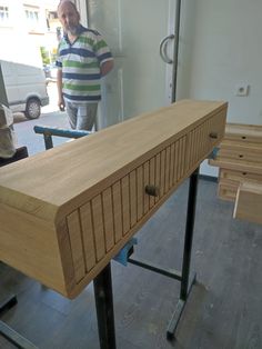 a man standing in front of a wooden table with metal legs and drawers on it