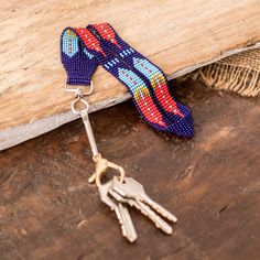 two keys are attached to a beaded keychain on a wooden surface with a piece of wood in the background