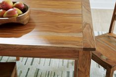 a bowl of fruit sitting on top of a wooden table next to a brown chair