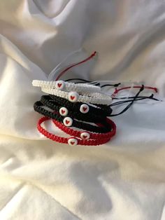 three bracelets with white and red beads on top of a white cloth covered sheet